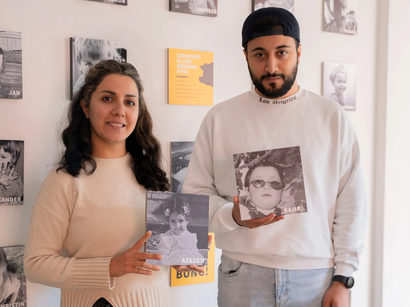 Azadeh und Bahri mit ihren Kinderfotos vor der Fotowand in der Agentur