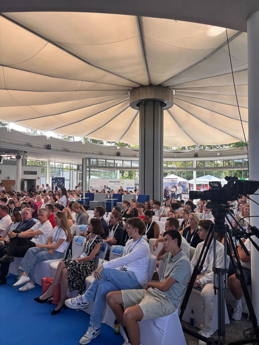 Publikum sitzt in Reihen unter einem Pavillon 