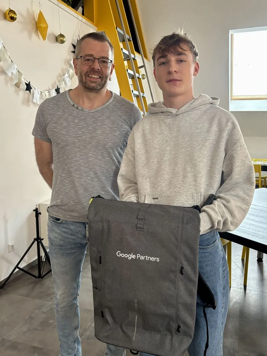 Andreas Bäuml (rechts) und Christian Walter (links) stehen in der Lounge der Werbeagentur. Andreas hält einen Google Partners-Rucksack in der Hand – ein Geschenk zur Anerkennung des neuen Google Partner Status der Agentur.