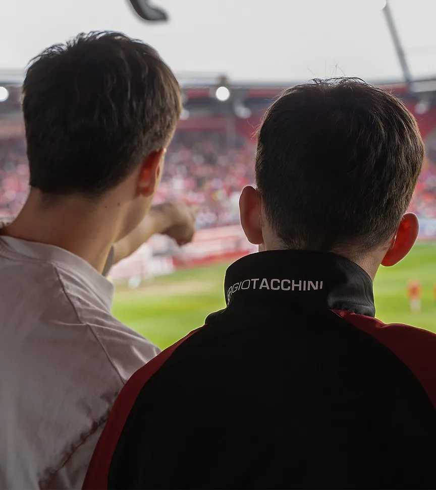 Zwei C3-Teammitglieder schauen von der Tribüne aus das SSV Jahn Spielfeld..